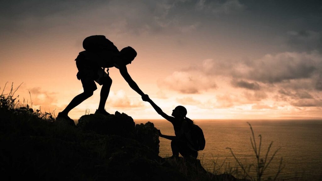 esempio di resilienza nelle relazioni sociali: due persone si aiutano a scalare una montagna